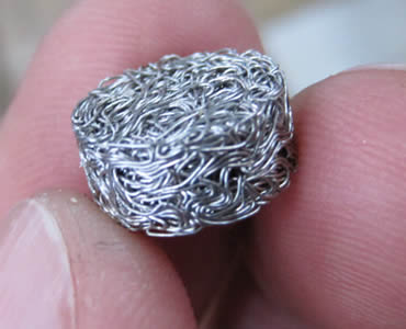 Fingers hold a small round knitted wire mesh filter made of compressed stainless steel mesh material.